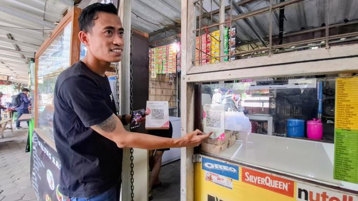 Salah satu pedagang, Karna (37) sedang menunjungakan barcode QRIS asli yang sempat ditempel dengan Barcode QRIS palsu.
