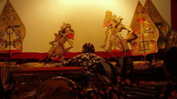KESENIAN WAYANG- Ilustrasi pertunjukan kesenian wayang, dimana seorang dalang sedang memainkan wayang dari balik layar pertunjukan.
