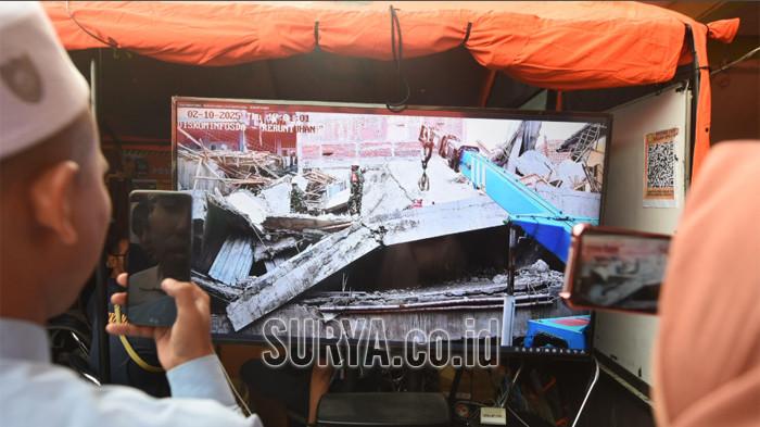 PANTAU DARI LAYAR - Keluarga memantau evakuasi korban bangunan runtuh di ponpes Al Khoziny, Buduran, Sidoarjo dari layar yang disediakan di posko Basarnas, Kamis (2/10/2025). Evakuasi korban bangunan runtuh mulai menggunakan alat berat.