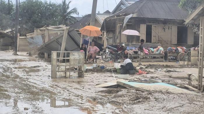 Warga di kawasan Kampung Durian Aceh Tamiang, terlihat menggunakan air kotor yang mengalir di antara lumpur tebal untuk mencuci pakaian. Foto direkam Minggu (7/12/2025).