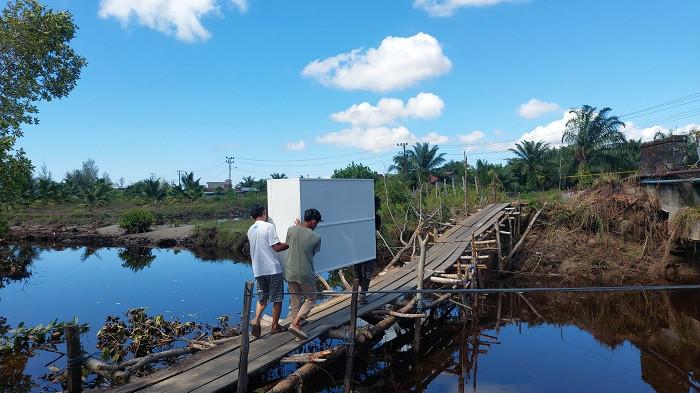 GOTONG BARANG: Warga gotong lemari melewati titian darurat akibat jalan putus di kawasan Gosong Telaga Barat, Singkil Utara, Aceh Singkil, Rabu (3/12/2025).