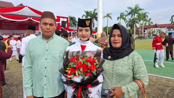 PEMBAWA BAKI - Pembawa baki Paskibraka Provinsi Babel, Resti, bersama kedua orang tuanya saat berada di halaman kantor Gubernur Babel, Minggu (17/8/2025).