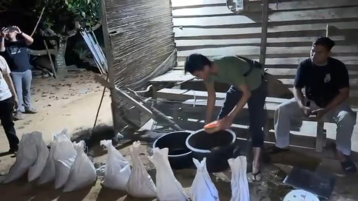 PENAMPUNGAN PASIR TIMAH - Anggota Satreskrim Polres Bangka Selatan memeriksa sejumlah karung berisi pasir timah saat penggerebekan di sebuah rumah di Desa Paku, Kecamatan Payung, Senin (2/3/2026) malam. Dalam operasi tersebut, polisi menemukan ratusan kilogram pasir timah beserta alat penimbangan dan penyaringan serta mengamankan seorang perempuan.