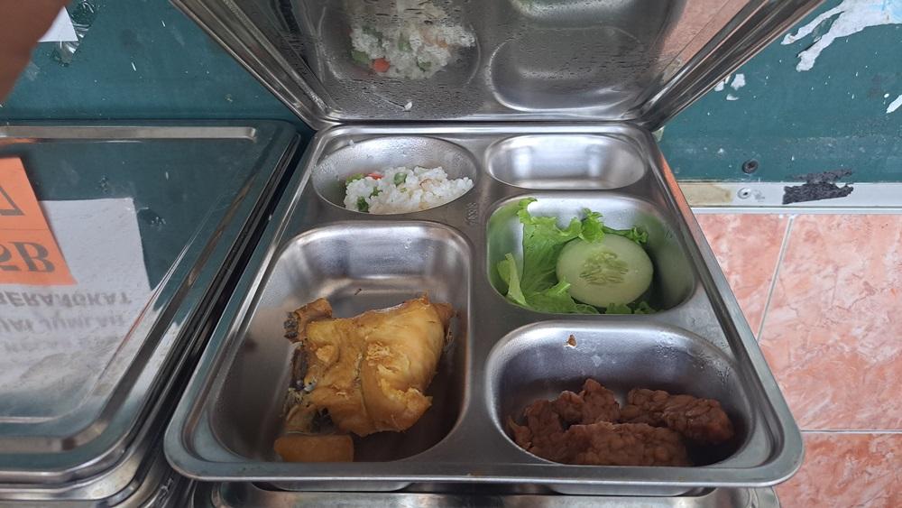 Ilustrasi petugas SPPG sedang memasang label batas waktu aman konsumsi pada kotak makanan bergizi gratis MBG di sebuah sekolah, dengan latar belakang anak-anak yang sedang makan dengan gembira.