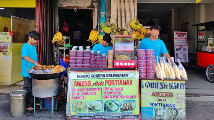 KULINER BOGOR – Suasana depan kedai Pisang Goreng Kalimantan Ameng, tampak aktivitas pegawai yang tengah menyiapkan aneka gorengan khas. Deretan pisang tanduk, ubi madu, serta wadah berisi sambal rujak dan pelengkap lainnya tertata rapi.