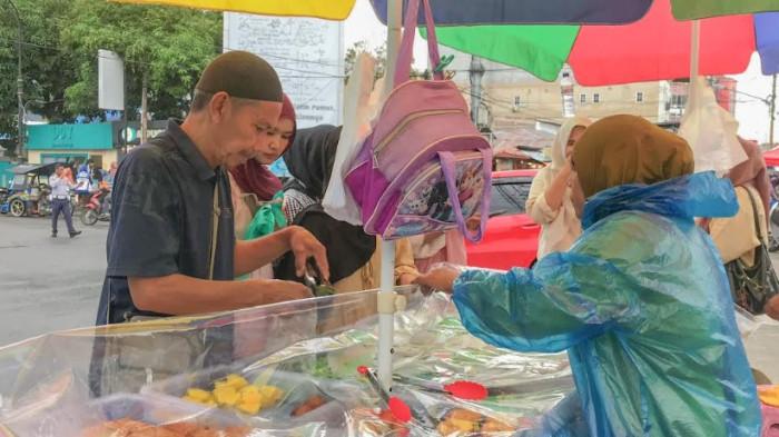 PENJUAL TAKJIL -- Hatim Mohammad saat melayani pembeli takjil. Hatim bersama suaminya menjajakan kue di kawasan Universitas Negeri Gorontalo.