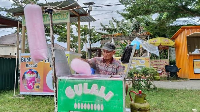 PENJUAL GULALI -- Ibrahim Pakaya alias Opa Bura saat berjualan gulali di Taman Kalimadu, Kota Gorontalo, Sabtu (28/2/2026). Opa Bura kini telah berusia 71 tahun.
