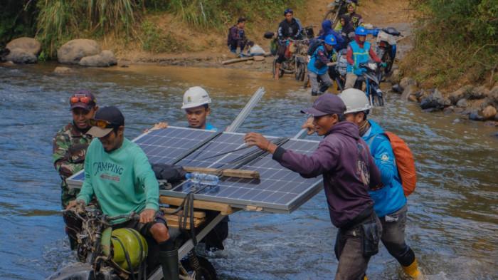 Petugas PLN bersama warga bahu-membahu membawa panel surya melintasi sungai