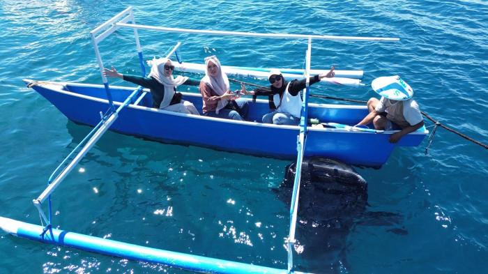 HIU PAUS -- Susi Sisanti Lasantu (mengenakan kerudung hitam) bersama teman-temannya saat berpose bersama hiu paus, Jumat (26/12/2025). Susi mengaku sudah tujuh kali mengunjungi wisata Hiu Paus Botubarani.