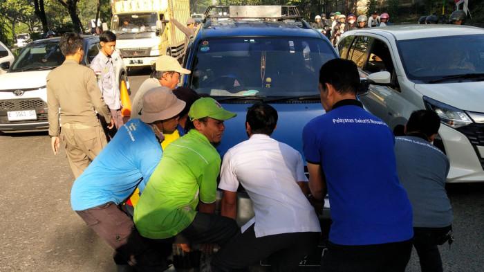 Sejumlah warga dan pegawai Kecamatan Panyileukan membantu mengevakuasi mobil Daihatsu Taruna yang tersangkut di atas marka Jalan Soekarno Hatta, Kota Bandung, Jawa Barat, Rabu (27/8/2025).