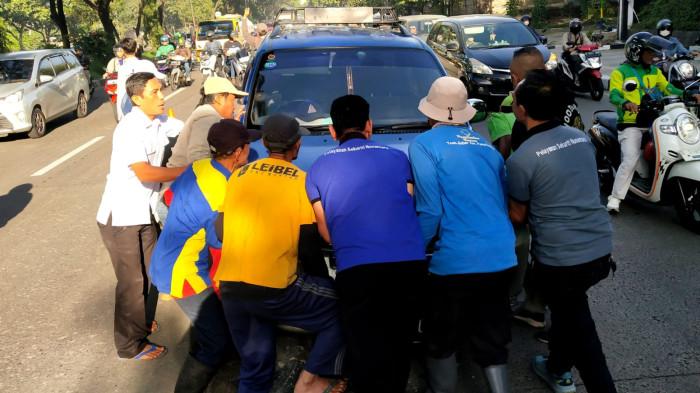Sejumlah warga dan pegawai Kecamatan Panyileukan membantu mengevakuasi mobil Daihatsu Taruna yang tersangkut di atas marka Jalan Soekarno Hatta, Kota Bandung, Jawa Barat, Rabu (27/8/2025).