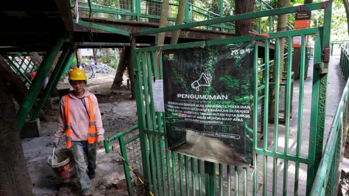 Seorang pekerja melintas di samping poster berisi pengumuman penutupan sementara taman hutan kota Babakan Siliwangi (Baksil) untuk umum yang dipasang di pintu keluar skywalk kawasan hutan kota Baksil, Kota Bandung, Jawa Barat, Kamis (16/10/2025).