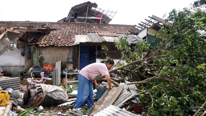 Seorang warga mengumpulkan puing-puing atap tempat parkiran yang ambruk dan dua orang membetulkan atap rumahnya yang rusak akibat disapu angin puting beliung, di RT 01, RW 07, Desa Pasanggrahan, Kecamatan Ujungberung, Kota Bandung, Jawa Barat, Rabu (5/11/2025).