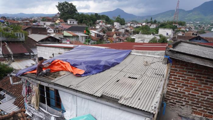 Seorang warga memasang terpal dari BPBD Kota Bandung di atap rumahnya yang sebagian rusak akibat disapu angin puting beliung, di RT 02, RW 07, Desa Pasanggrahan, Kecamatan Ujungberung, Kota Bandung, Jawa Barat, Rabu (5/11/2025).
