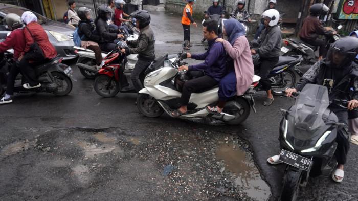 Kendaraan bermotor melintasi permukaan jalan rusak yang digenangi air di Jalan Terusan Cibaduyut, Kabupaten Bandung, Jawa Barat, pada Sabtu (22/11/2025).