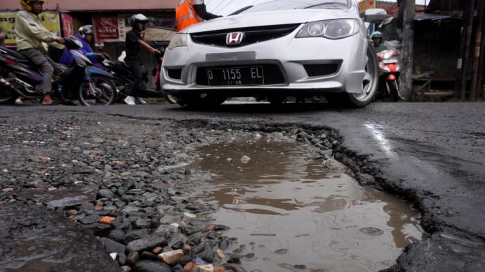 Kendaraan bermotor melintasi permukaan jalan rusak yang digenangi air di Jalan Terusan Cibaduyut, Kabupaten Bandung, Jawa Barat, pada Sabtu (22/11/2025).