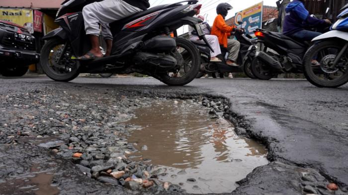Kendaraan bermotor melintasi permukaan jalan rusak yang digenangi air di Jalan Terusan Cibaduyut, Kabupaten Bandung, Jawa Barat, pada Sabtu (22/11/2025).
