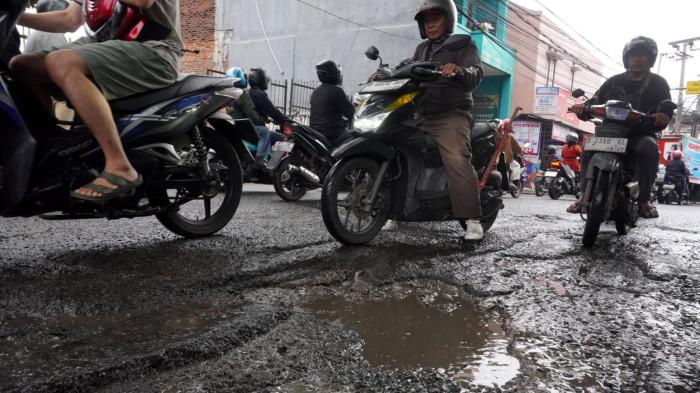 Kendaraan bermotor melintasi permukaan jalan rusak yang digenangi air di Jalan Terusan Cibaduyut, Kabupaten Bandung, Jawa Barat, pada Sabtu (22/11/2025).