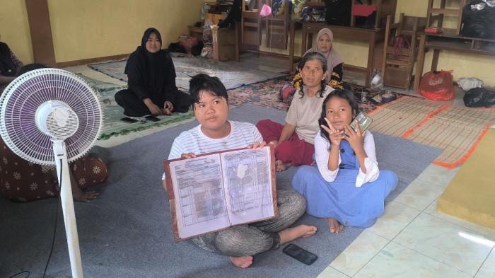 RAPOR TERENDAM BANJIR - Asila Apriliani (11) menunjukkan buku rapornya yang rusak setelah terendam banjir akibat jebolnya tanggul Sungai Cijengkol di Perumahan Grand Texpia, Kabupaten Subang, Minggu (25/1/2026).