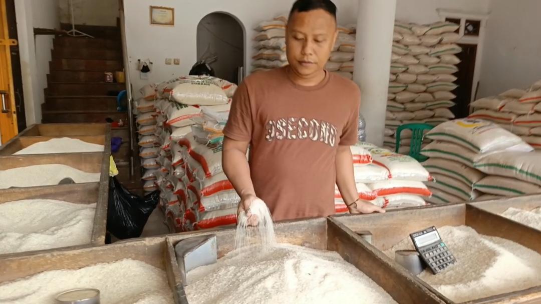 Sawah padi yang luas dan subur di Indramayu, Jawa Barat, dengan petani sedang melakukan aktivitas menanam atau merawat padi di bawah langit biru cerah, menunjukkan suasana pertanian yang produktif.