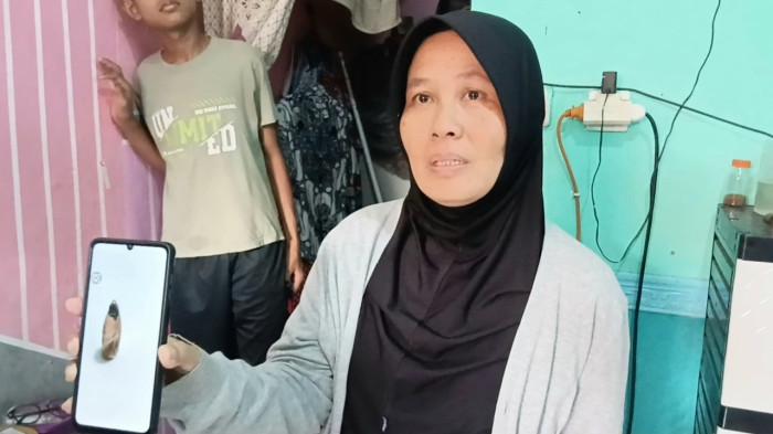 PELURU NYASAR - Pemilik rumah, Hamidah saat menunjukkan foto proyektil peluru yang menembus rumahnya di Ciracas, Jakarta Timur, Rabu (20/5/2026). TRIBUNJAKARTA.COM/BIMA PUTRA