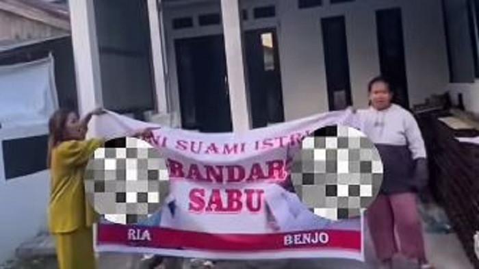 GERUDUK RUMAH - Aksi emak-emak geruduk rumah bandar narkoba. Bukan sekadar datang berdemo, sekelompok emak-emak ini membawa 'senjata' psikologis yang mematikan bagi buronan: sebuah spanduk cetakan berukuran raksasa yang secara gamblang memampang foto wajah serta identitas pasangan suami istri (pasutri) pemilik rumah yang dituding sebagai bandar sabu.