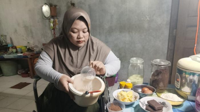 KEMBALI PRODUKTIF - Bunga Kurniaputri Arida (26) duduk di kursi roda sembari membuat kue di rumah untuk dijual daring, Jumat (28/11/2025) malam. Pekerja lapangan sebuah kantor cabang bank di Demak, Jawa Tengah, tengah menjalani aktivitas WFH sembari mulai menekuni usaha kuliner.