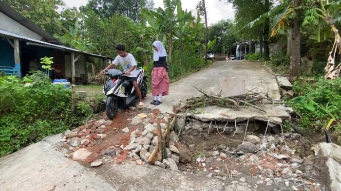 TANAH GERAK - Warga berjalan hati-hati di atas jalan kampung yang bagian bawahnya sudah ambles dan menganga di Kampung Sekip, Jangli, Kota Semarang, Kamis (5/2/2026). Pergerakan tanah menyebabkan retakan memanjang dan melebar, membuat jalan tidak lagi stabil dan berisiko runtuh jika dilewati kendaraan berat.