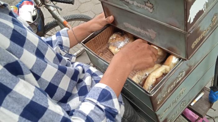 Daud sedang mengambilkan pesanan roti hangat untuk pembeli di Jalan Prawirotaman, Selasa (18/11/2025).