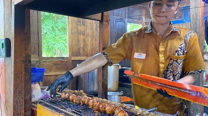 BAKSO BAKAR KEJU - Seorang karyawan sedang menyajikan bakso bakar keju setengah meter, di warung Bakso Pikat, Ring Road Selatan, Kapanewon Kasihan, Kabupaten Bantul, Minggu (21/12/2025).