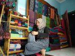 dwi-sulistyowati-istri-pemilik-usaha-pakel-arum-tampak-berbagai-karya-tenun-di-belakangnya.jpg