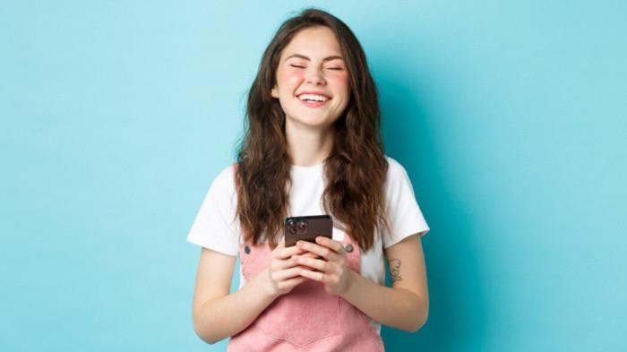 PANTUN PUJIAN - Potret wanita tertawa memegang handphone dari Freepik.com, Senin (5/8/2025). Simak kumpulan pantun pujian buat si cantik berikut ini, cara seru sampaikan rayuan ke pacar atau gebetan.