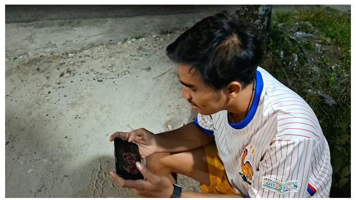 ENONTON - Fajar, satu di antara penjaga parkir di sebuah kafe Jalan Janah Jari, Palangka Raya menyempatkan diri menonton sepak bola di tengah kesibukkannya, Sabtu (30/5/2026).