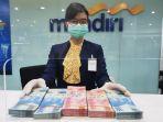 karyawati-bank-mandiri-sedang-memperlihatkan-pecahan-uang-yang-akan-ditukarkan-jelang-lebaran.jpg