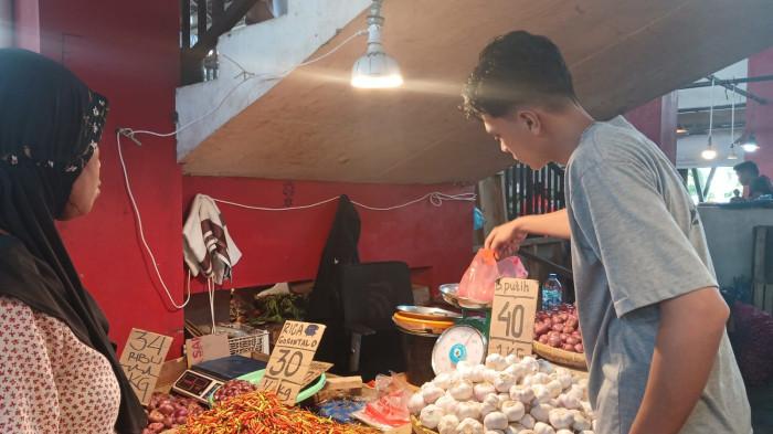 PEDAGANG - Pedagang barito di Pasar Bersehati Manado, Fikri, melayani pembeli, Minggu (8/2/2026). Sejumlah harga bahan pangan naik hari ini.