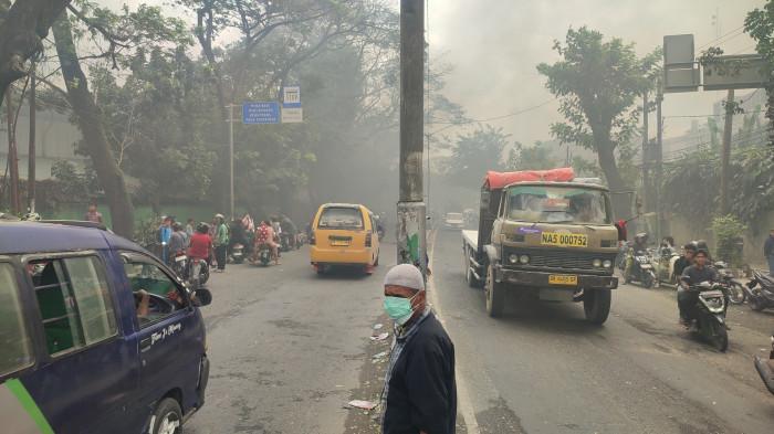 ASAP GANGGU PENGENDARA - Charli, pengemudi ojek online mengenakan masker saat melihat TKP pabrik sandal yang terbakar, di Jalan KL Yos Sudarso, Kecamatan Medan Deli, Kota Medan, Rabu (28/1/2026). Tebalnya asap yang sudah menutupi jalan, mulai menggangu aktivitas masyarakat maupun pengendara yang melintas.