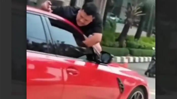 PRIA BERGELANTUNGAN - Seorang pria bergelantungan di kap mobil di kawasan Grogol Petamburan, Jakarta Barat, Jumat (1/5/2026) sekitar pukul 14.30 WIB. Polisi masih menyelidiki penyebab keributan tersebut.