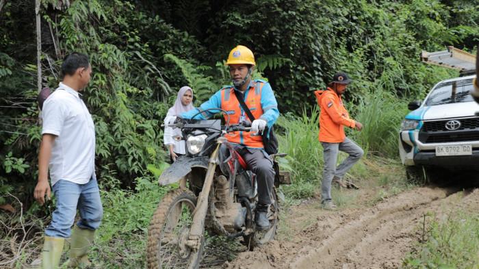 Petugas Pelayanan Teknik dibantu diarahkan oleh perangkat desa saat melintasi jalan berlumpur,