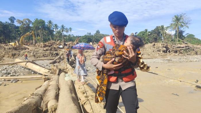 GENDONG BAYI - Seorang polisi menggendong bayi saat melintasi jembatan darurat di Garoga, Batangtoru, Kamis (4/12/2025). Di atas jembatan ini merupakan Desa Garoga yang sudah hilang diterjang banjir bandang.