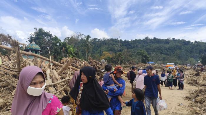 LEWATI KAYU - Warga berjalan melewati tumpukan kayu sisa banjir bandang yang melanda Garoga, Batangtoru, Tapsel, Kamis (5/12/2025).