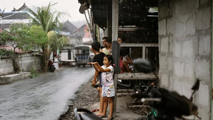 MENUNGGU REDA- Seorang bocah dan beberapa orang lainnya yang sedang berada di pinggir jalan Kota Bali sedang menunggu hujan reda. Mereka berteduh di gubuk kecil.