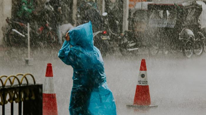 HUJAN LEBAT- Ilustrasi seorang pejalan kaki tampak menggunakan mantel plastik saat berusaha menembus hujan lebat.