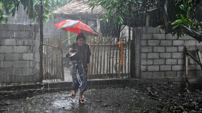 HUJAN SEDANG- Ilustrasi seorang wanita sedang berjalan membawa payung menembus hujan sedang yang melanda kawasan tempat tinggalnya.