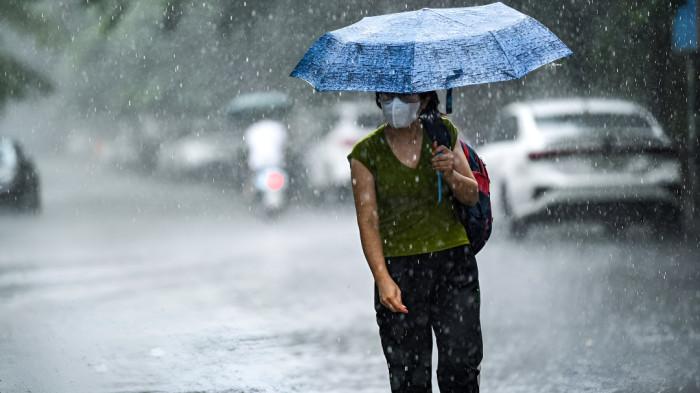 HUJAN SEDANG- Seorang wanita tampak menggunakan payung di tengah kondisi cuaca hujan sedang.