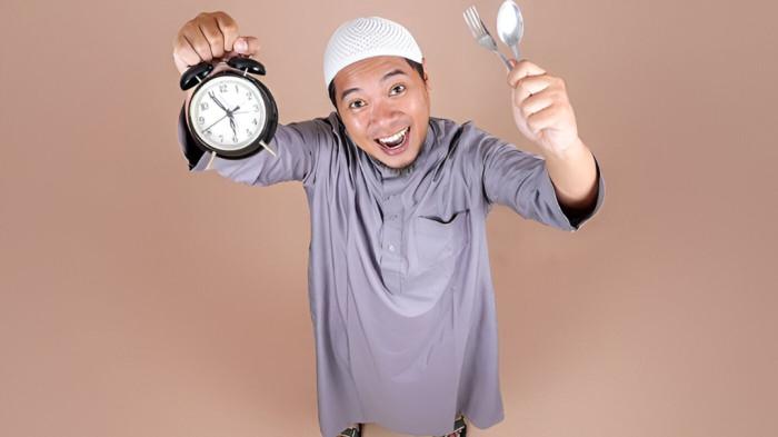 IMSAKIYAH- Ilustrasi imsakiyah Ramadhan, yang diperagakan seorang pria berpakaian muslim sedang memegang sebuah jam sebagai penanda waktu.