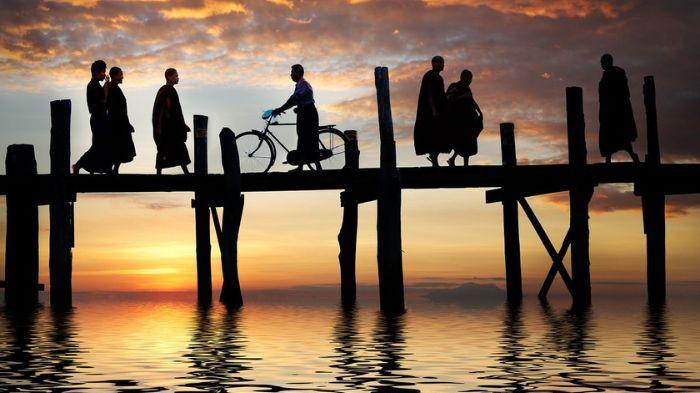 MELINTASI JEMBATAN- Tampak sejumlah bhiksu dan masyarakat melintasi sebuah jembatan yang ada di sebuah sungai. Jembatan itu ditopang oleh kayu laut.