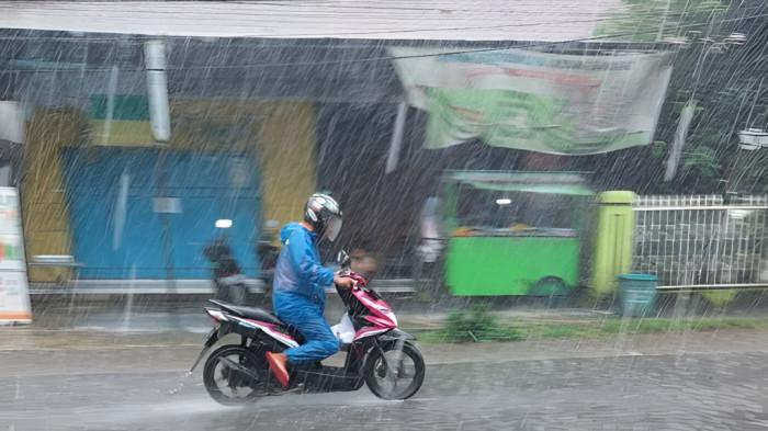 HUJAN LEBAT- Seorang pengendara motor tampak menembus hujan lebat menggunakan mantel di siang hari.