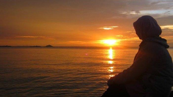 Potret wanita tengah memandang lautan setelah matahari terbenam.