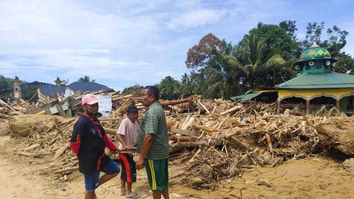 BERBINCANG -  Warga berbincang di tengah puing-puing kayu gelondongan pascabanjir bandang di Garoga, Batangtoru, Tapsel, Kamis (4/12/2025). Banjir ini menyapu rumah-rumah warga sampai nyaris kondisi desa nyaris hilang.