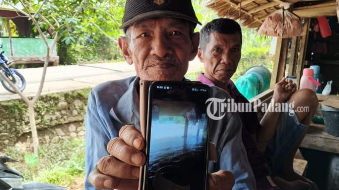BANJIR PADANG PARIAMAN - Basri (67) warga Korong Surantih, Nagari Lubuak Alung, Kecamatan Lubuk Alung, Kabupaten Padang Pariaman, melihat foto banjir yang merendam rumahnya pada Jumat (2/1/2026) lalu. Banjir yang kerap terjadi setiap hujan turun membuat warga setempat hidup dalam kecemasan.